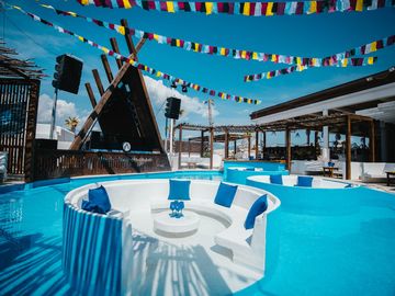 Round pool with white lounge islands under the flags – Nomad Beach Club, Zrce Beach