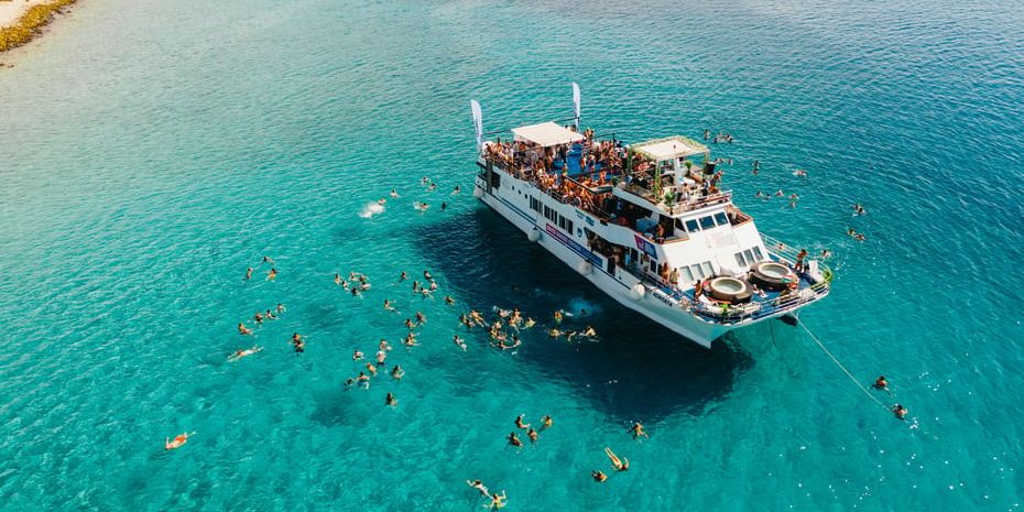 Zrće Booze Cruise party boat anchored in turquoise sea, people swimming around it